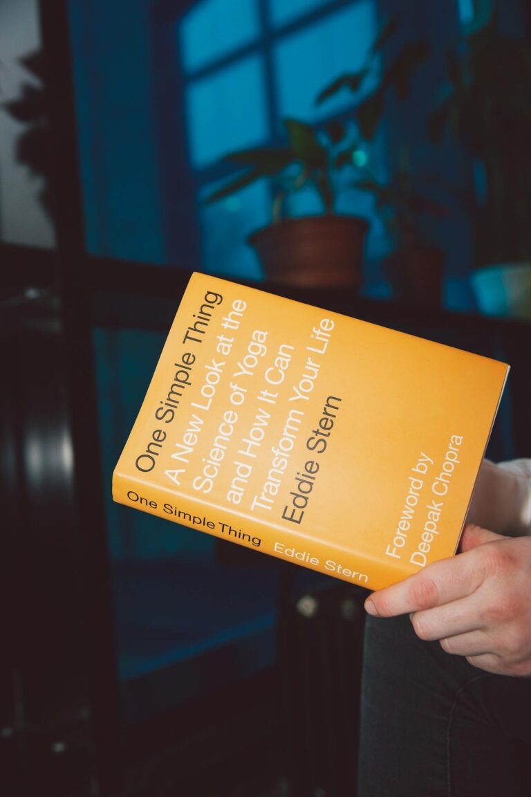 A person holding a yoga science book titled 'One Simple Thing' indoors.